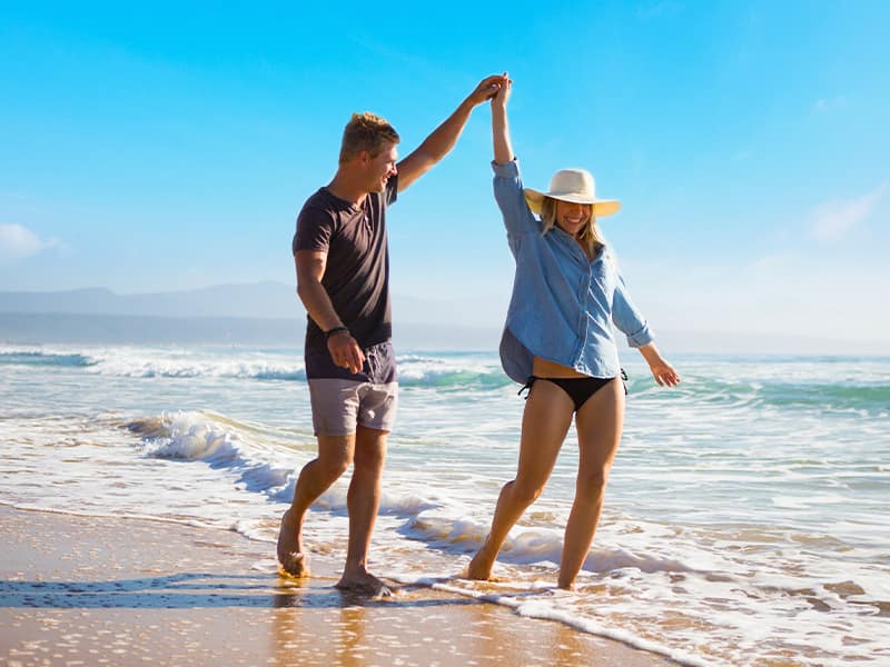 Man and women couple holding hands while walking on the beach during cruise tour